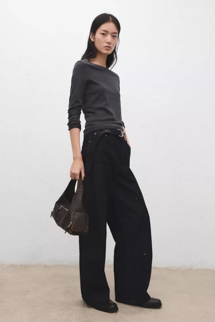 Woman in a dark long-sleeve top and wide-leg pants holding a shoulder bag