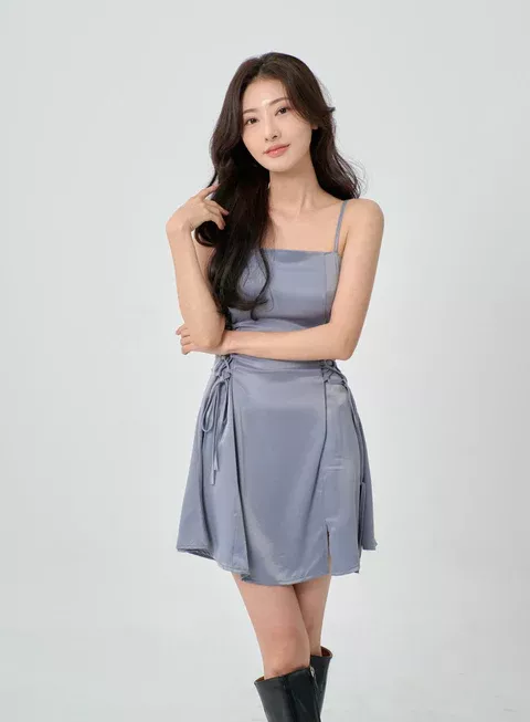 Woman with long dark hair in a blue dress and black boots posing in a studio