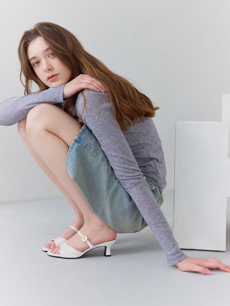 Woman with long hair in a gray top and denim skirt, squatting indoors