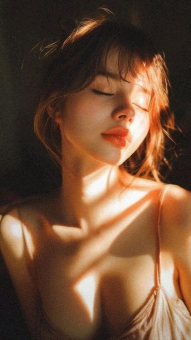 Woman with red hair and closed eyes, illuminated by warm, dramatic lighting