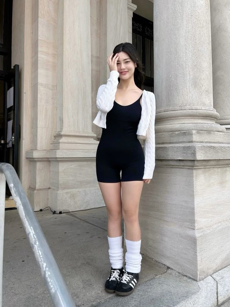 Woman in a black romper and white cardigan posing outdoors