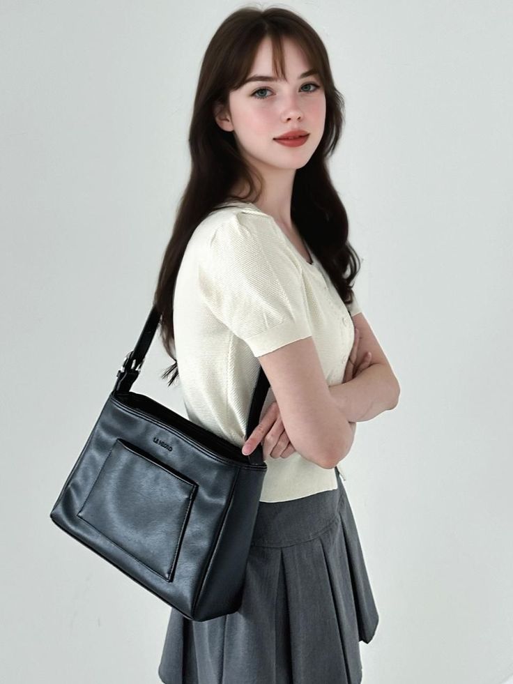 Woman with long dark hair and bangs wearing a white top and gray pleated skirt