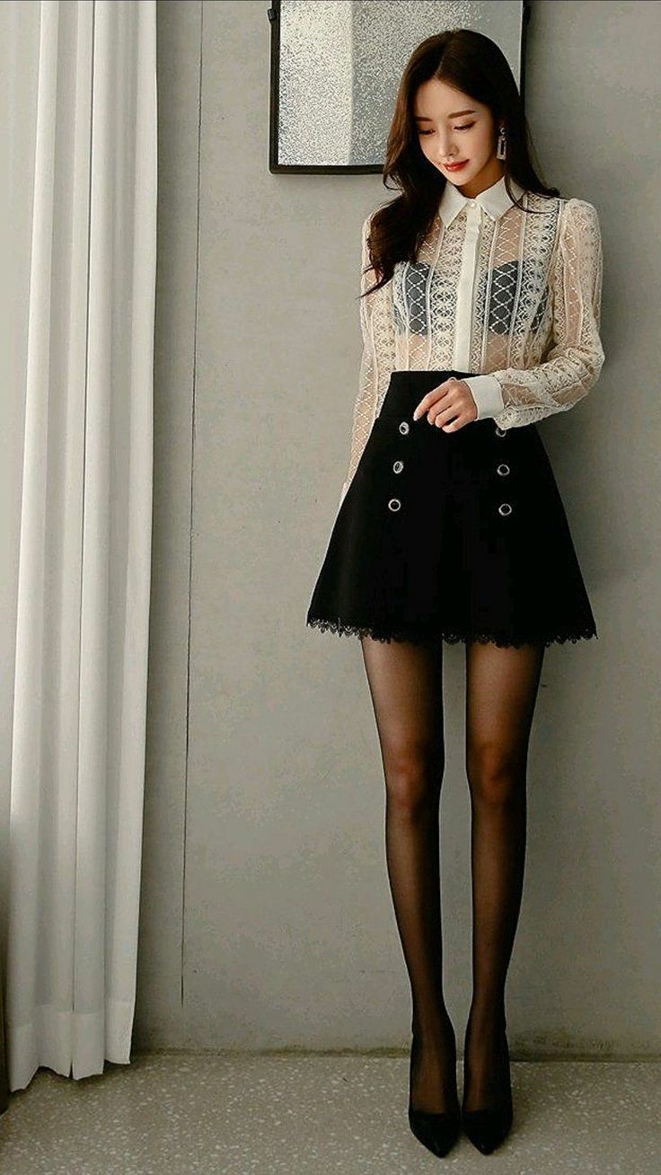 Woman in a lace shirt, black skirt, and black tights posing indoors