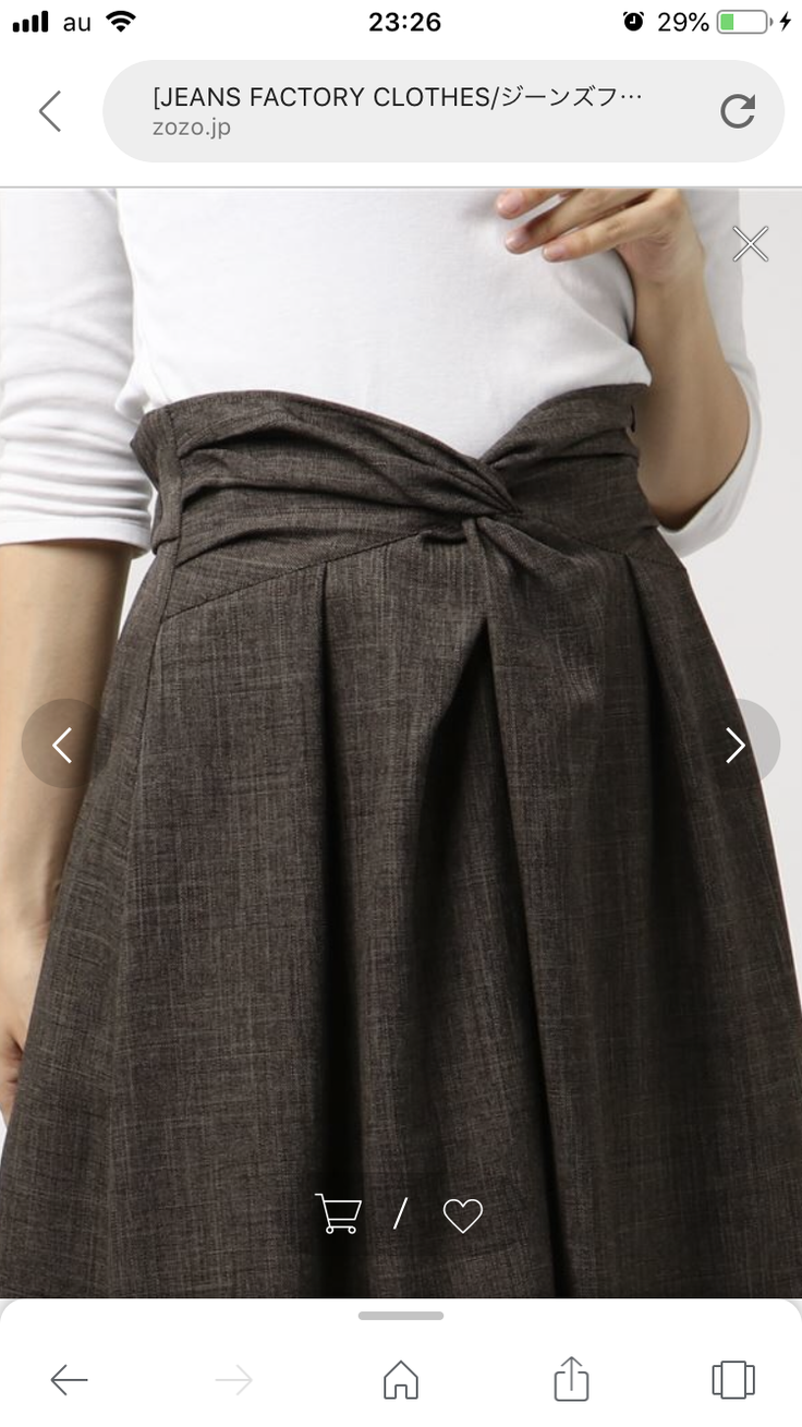 Woman wearing a brown high-waisted pleated skirt with a knot detail and a white top