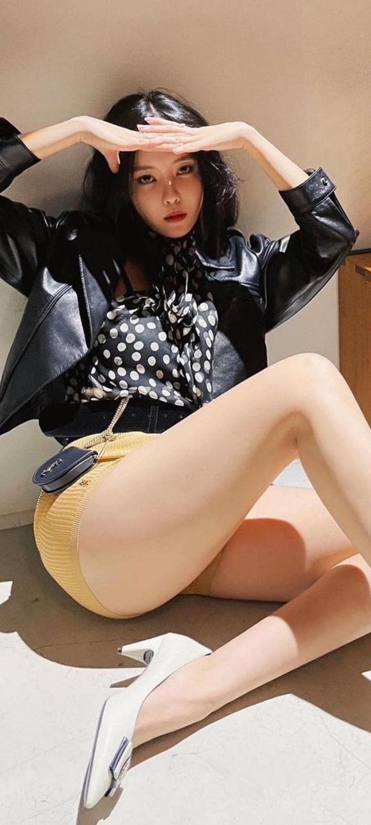 Woman in a black leather jacket and yellow shorts posing indoors