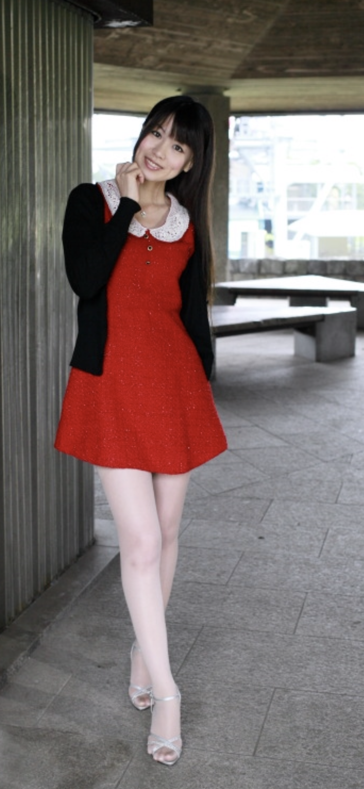 Woman in a red dress and black cardigan smiling outdoors