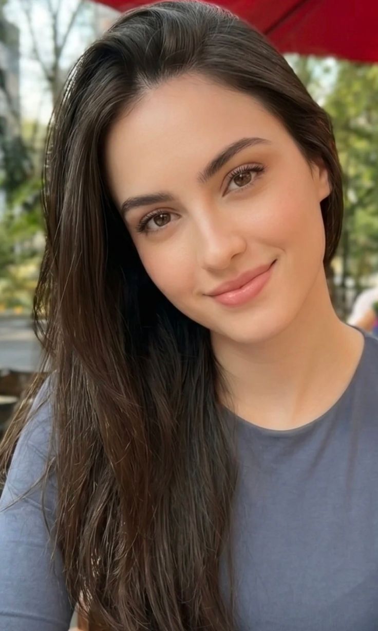 Woman with long brown hair smiling outdoors with soft lighting