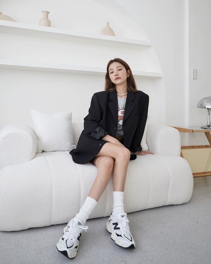 Woman in a black blazer and sneakers sitting on a white couch indoors