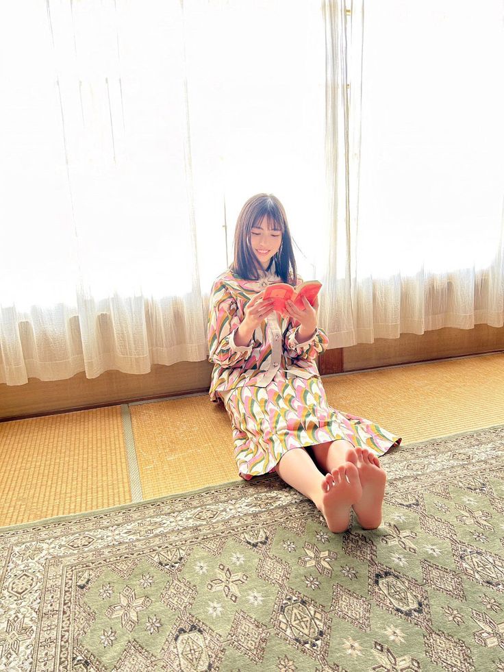 Woman in a colorful patterned dress sitting on a tatami mat and reading a book