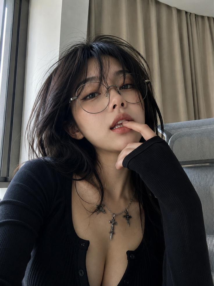 Woman with black hair and glasses wearing a black top and cross necklace