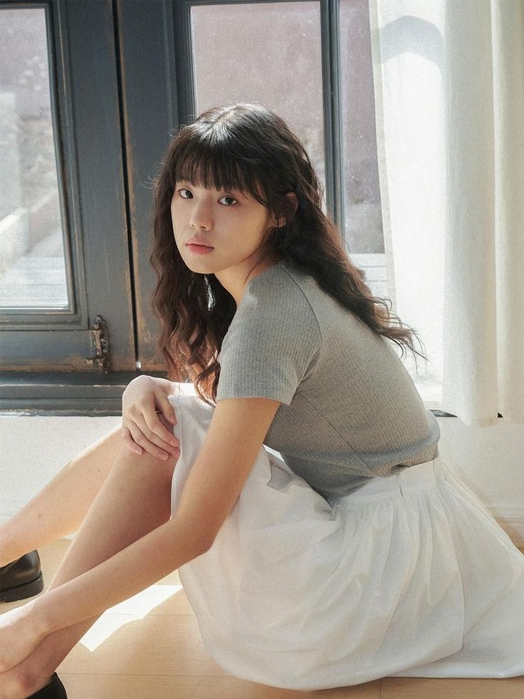 Woman with long wavy hair and bangs sitting on the floor by a window