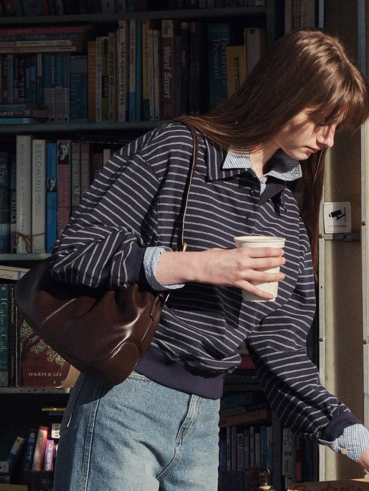 Woman in a striped shirt and jeans holding a cup in front of a bookcase