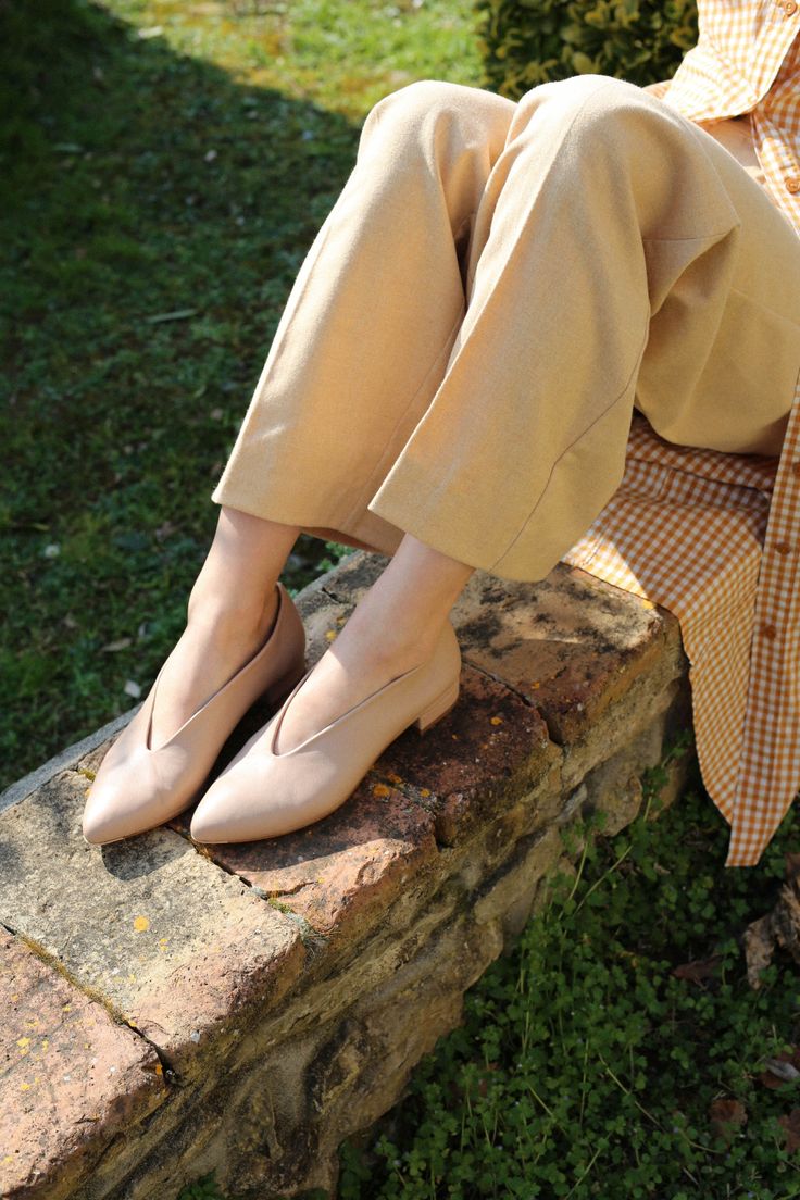 Person wearing beige pants and nude flats sitting on a brick wall outdoors