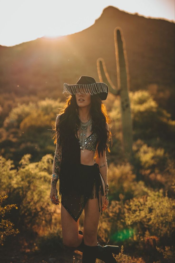 Woman in a cowboy hat and fringed outfit in a desert landscape at golden hour