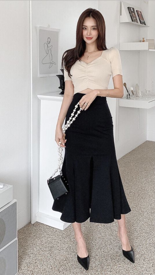 Woman in a beige crop top and black midi skirt holding a pearl strap bag