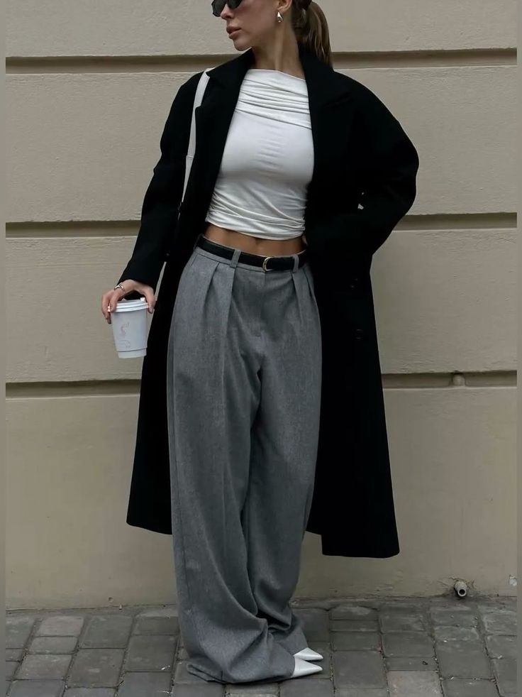 Woman in a black coat, crop top, and wide leg pants holding a coffee cup