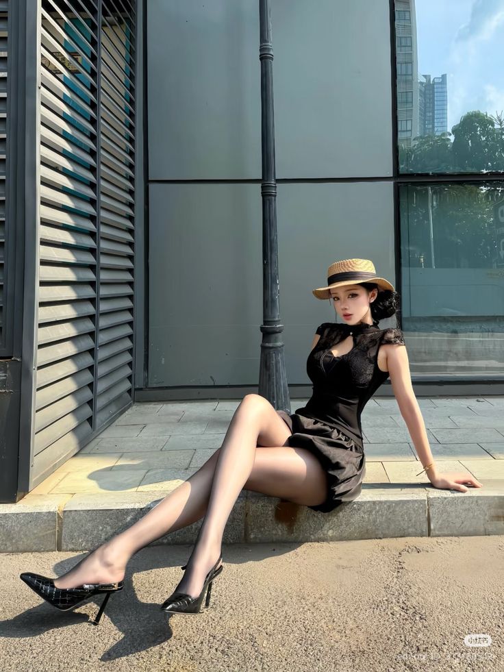 Woman in a black dress and straw hat sitting on a curb outdoors