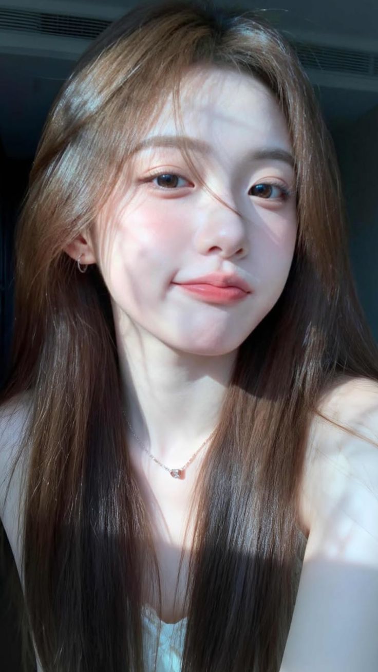 Woman with long brown hair and a necklace, illuminated by soft sunlight