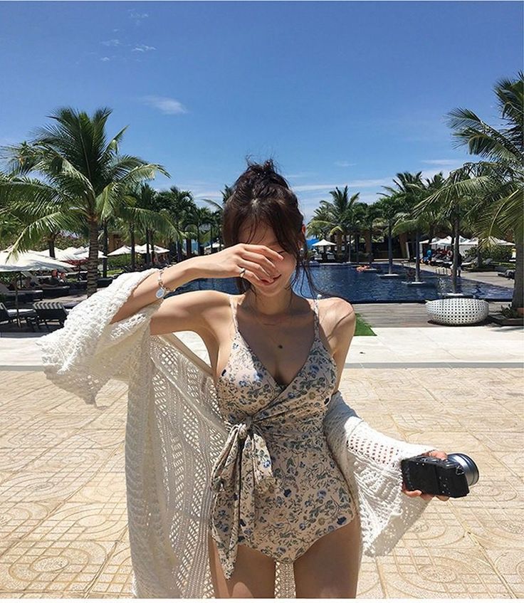 Woman in a floral swimsuit and long cardigan by a swimming pool