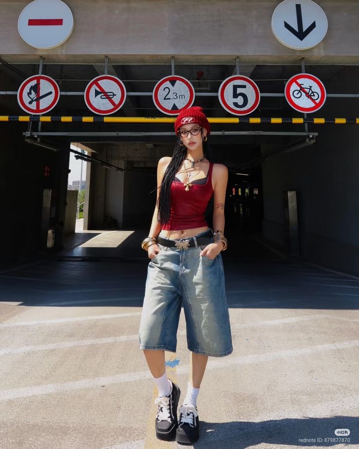 Woman in a red tank top and denim shorts standing in an urban setting