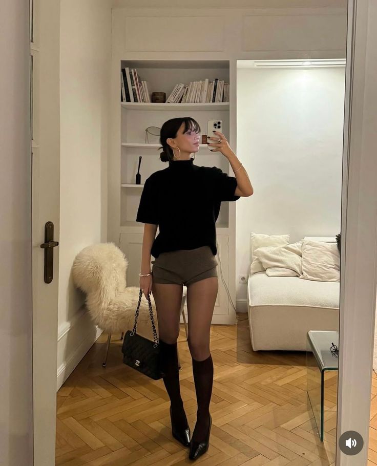 Woman in a black top and shorts taking a mirror selfie indoors
