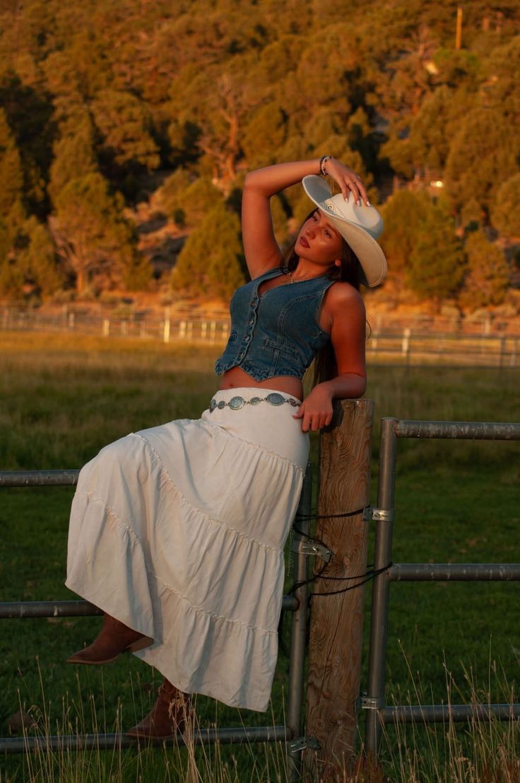 Woman in a cowboy hat and denim vest posing on a fence at golden hour