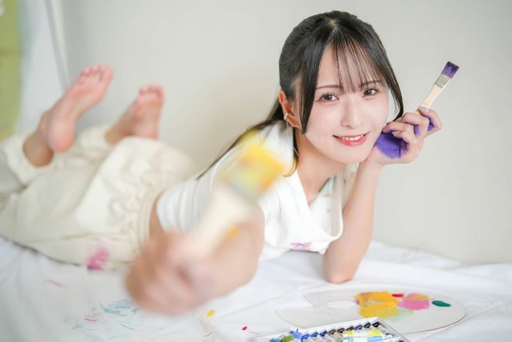 Woman with paint on her hands holding brushes and smiling while lying down