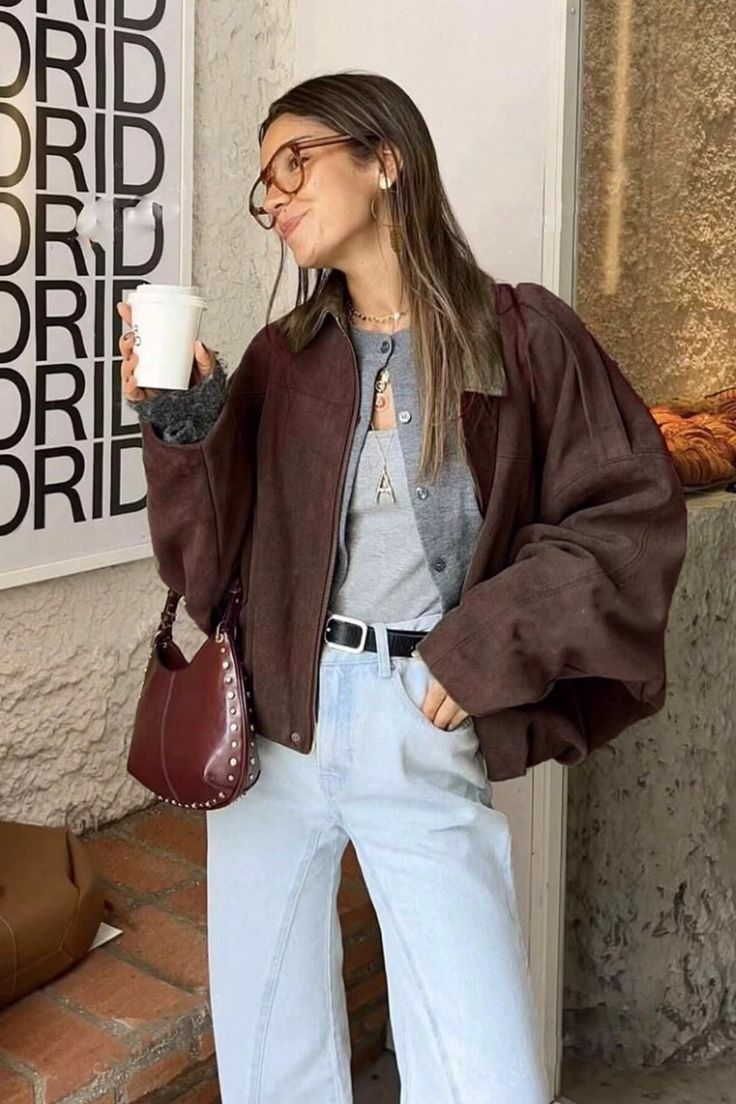 Woman in a brown jacket and light wash jeans holding a coffee cup