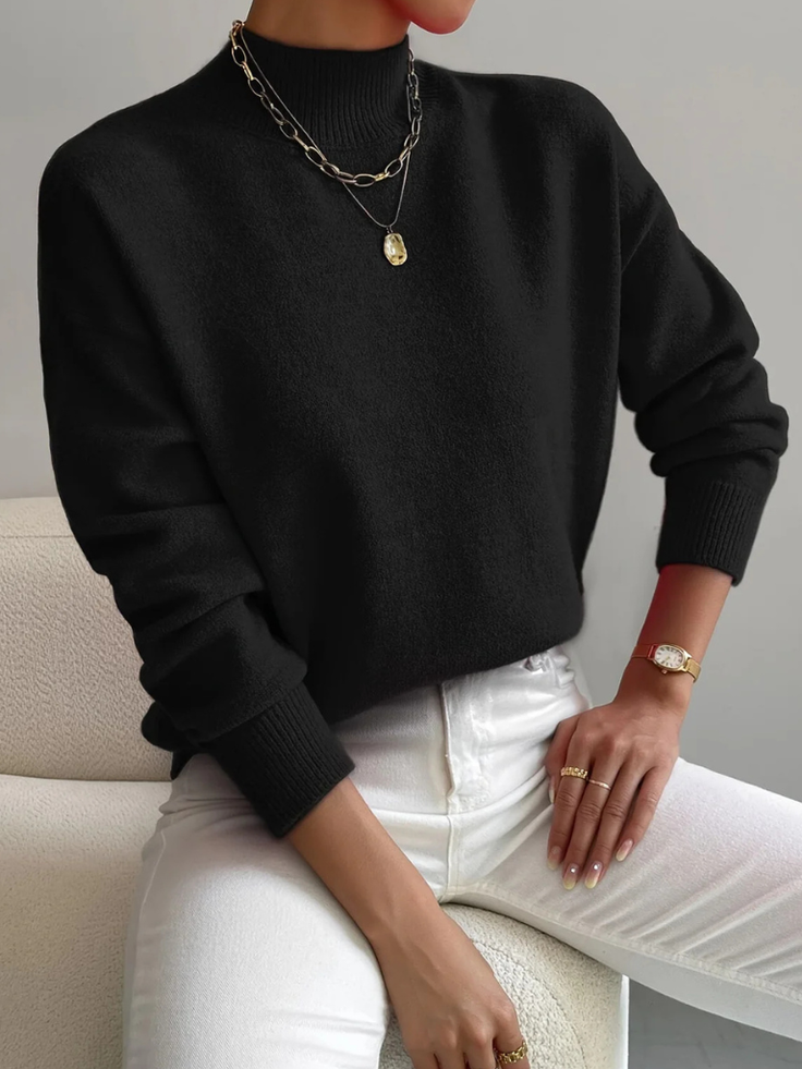 Person in a black sweater and white pants with gold jewelry