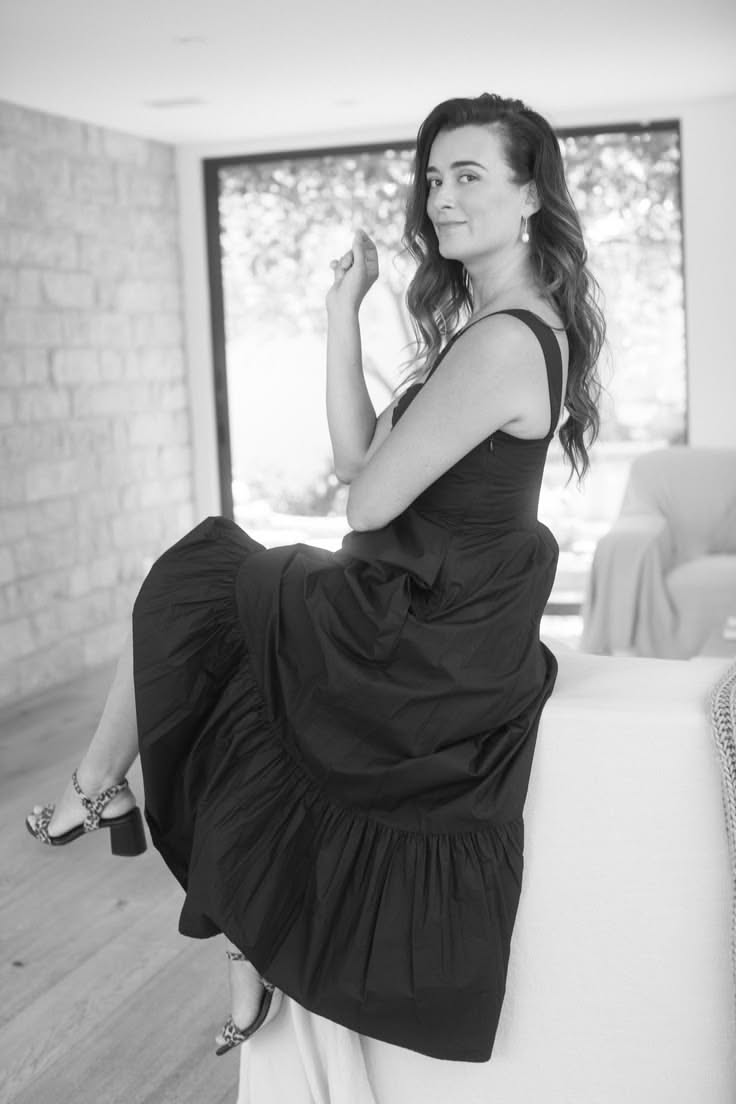 Woman in a black dress and leopard print heels sitting indoors