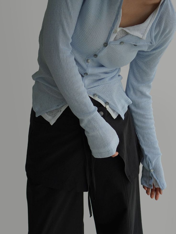 Person in a light blue cardigan and black pants, bending forward