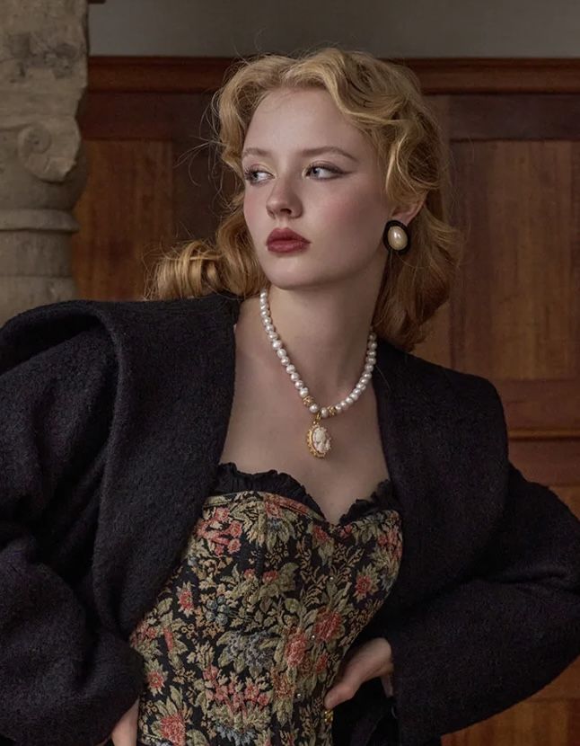 Woman with blonde wavy hair wearing a floral corset and pearl necklace