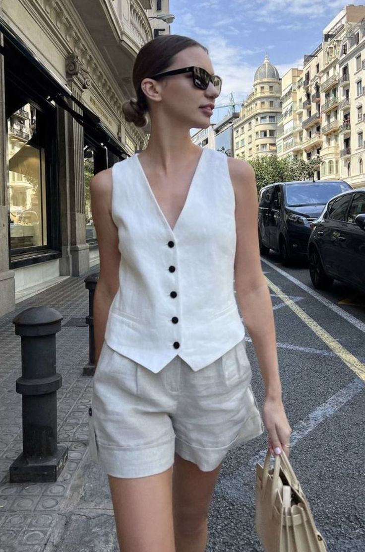 Woman in a white vest and linen shorts walking on a city street