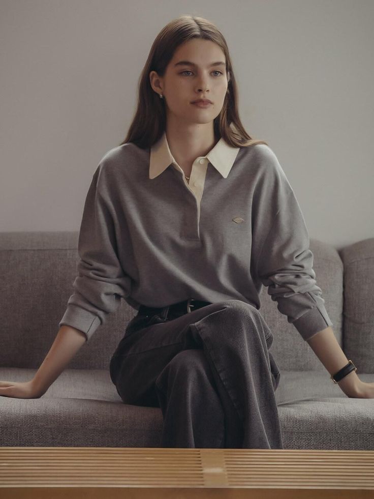 Woman with long hair wearing a gray polo shirt and jeans, sitting on a sofa