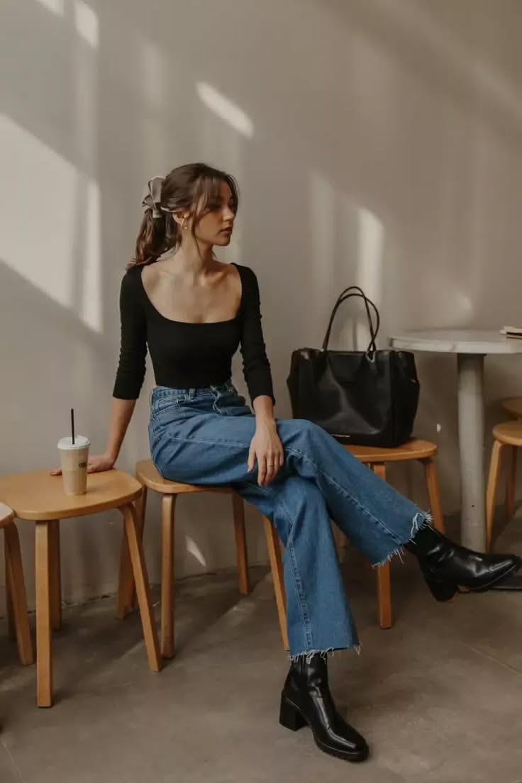 Woman in a black top and blue jeans sitting indoors with a coffee cup