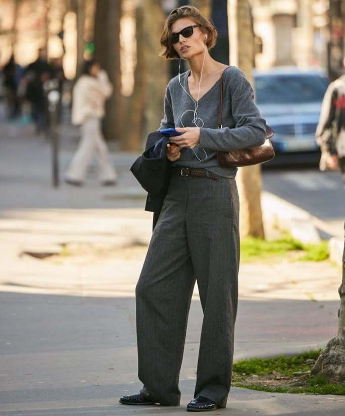 Woman with short hair and sunglasses wearing a sweater and wide leg pants on a street