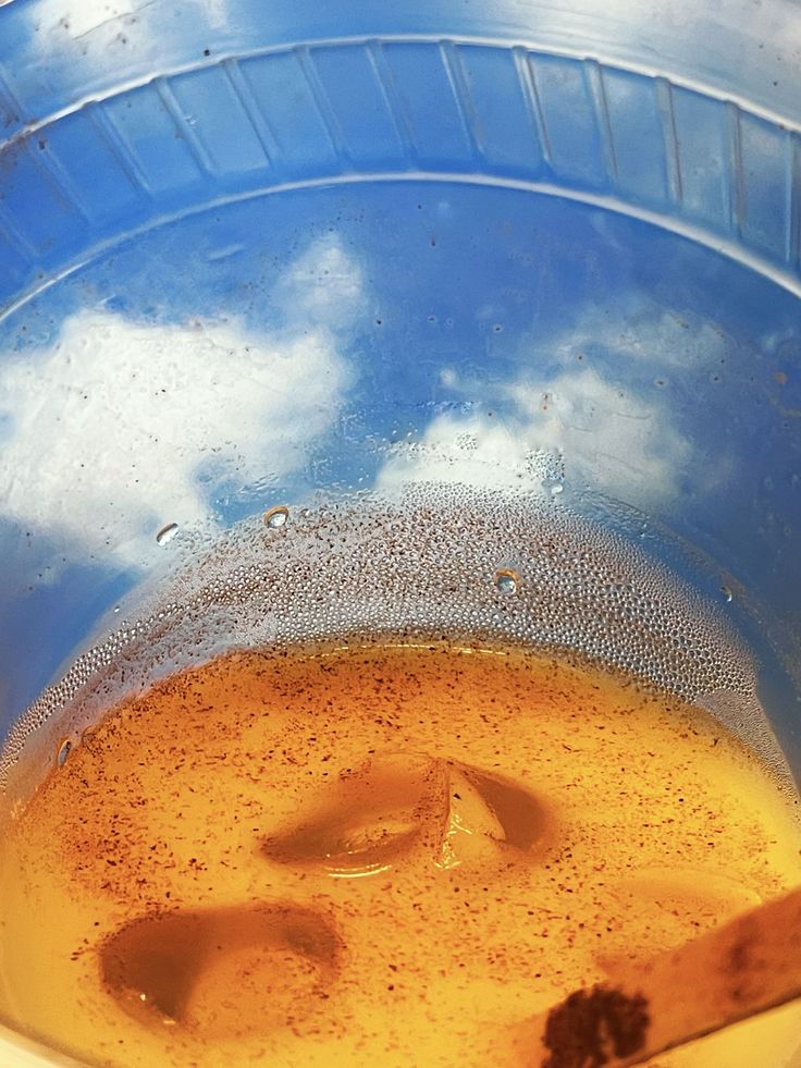 Orange liquid with ice cubes in a blue bucket reflecting the sky