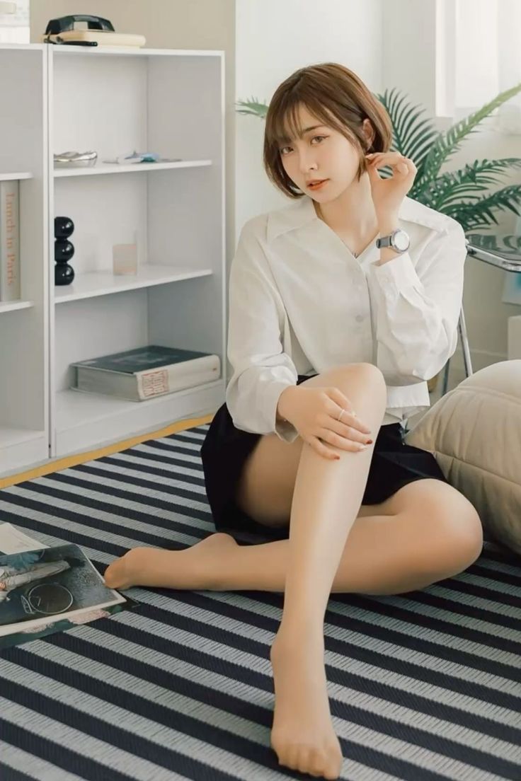 Woman with short hair wearing a white shirt and black skirt, sitting on a striped rug
