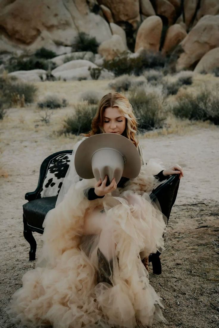 Woman in a tulle dress and cowboy hat sitting in a desert landscape