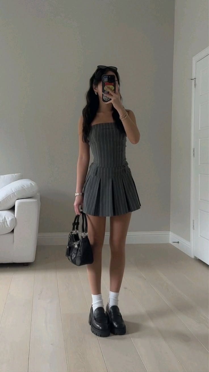 Woman in a pinstripe dress holding a black handbag, taking a mirror selfie