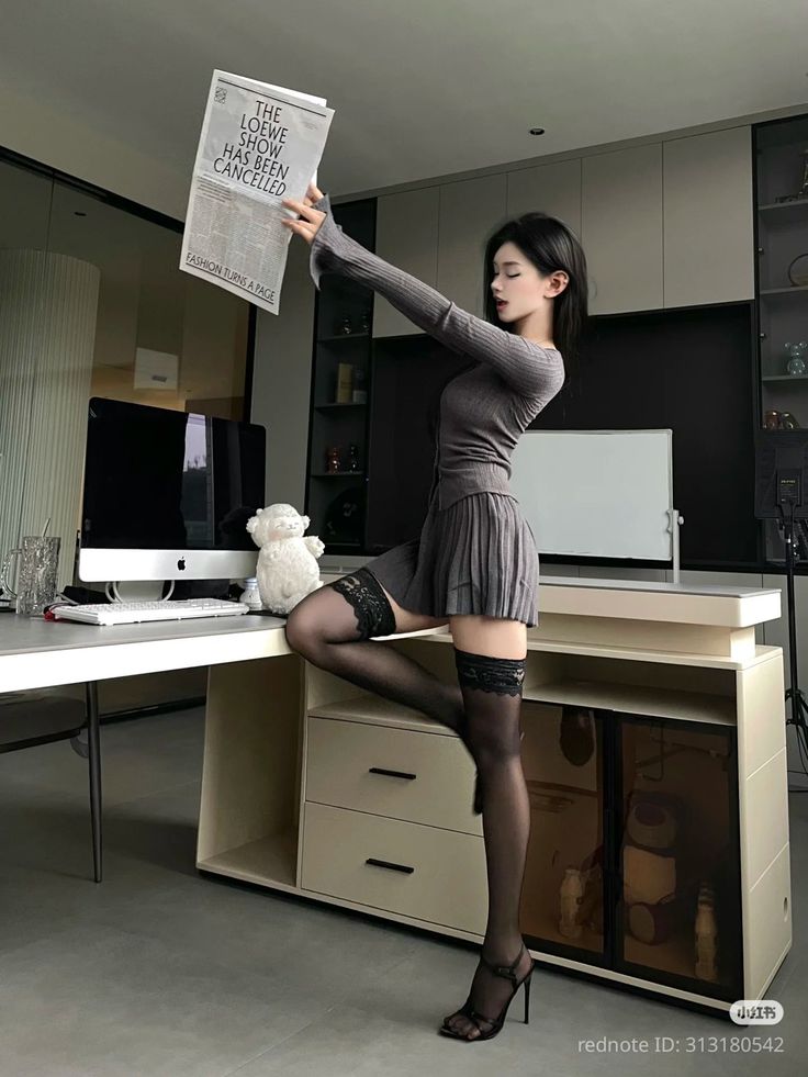 Woman in a gray dress and thigh-high stockings posing in an office