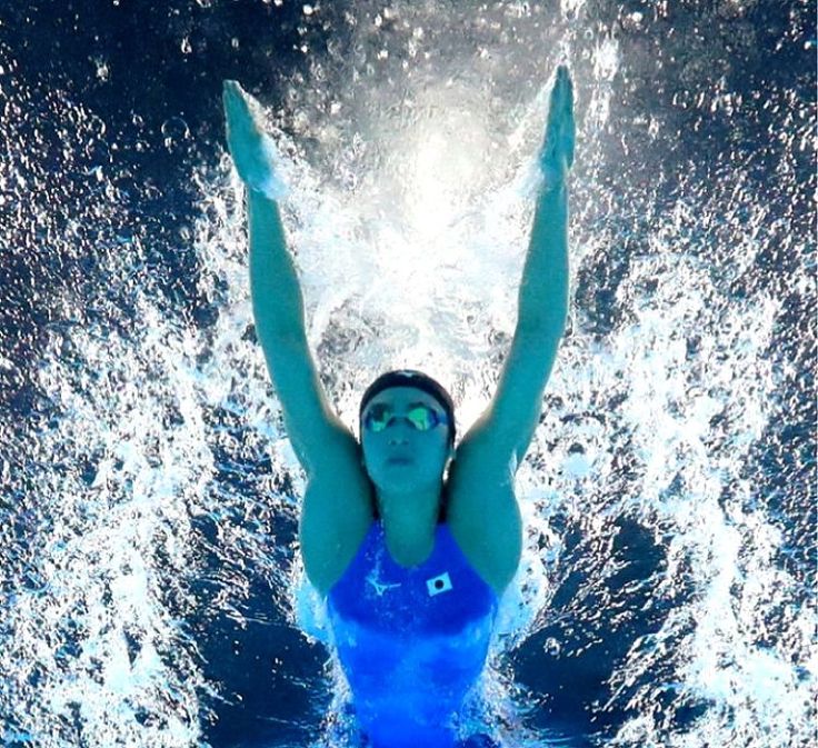Swimmer in a blue swimsuit and goggles underwater with arms raised