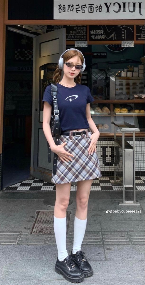 Woman in a plaid skirt and crop top with pigtails and headphones outdoors