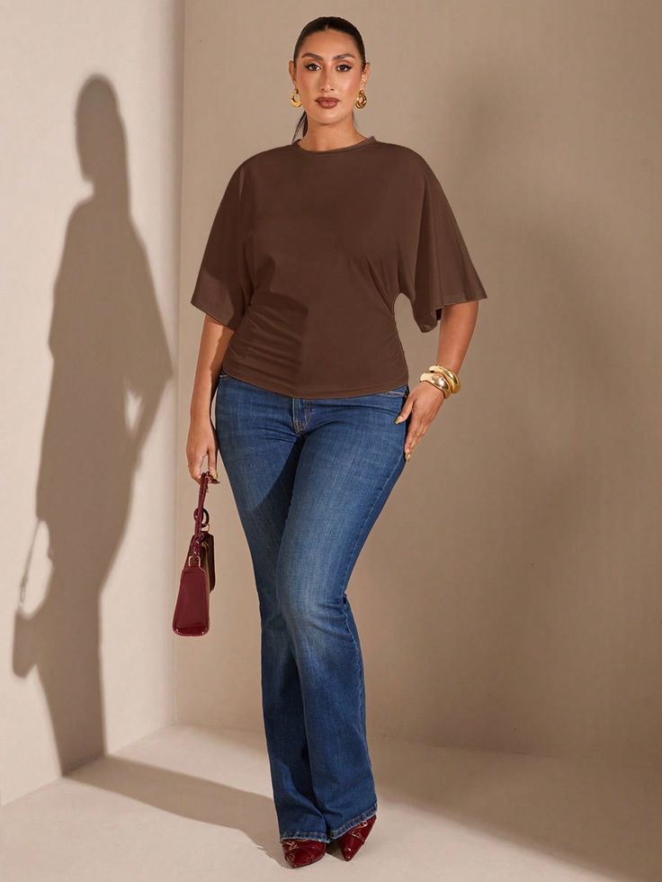 Woman in a brown top and blue jeans holding a red handbag indoors