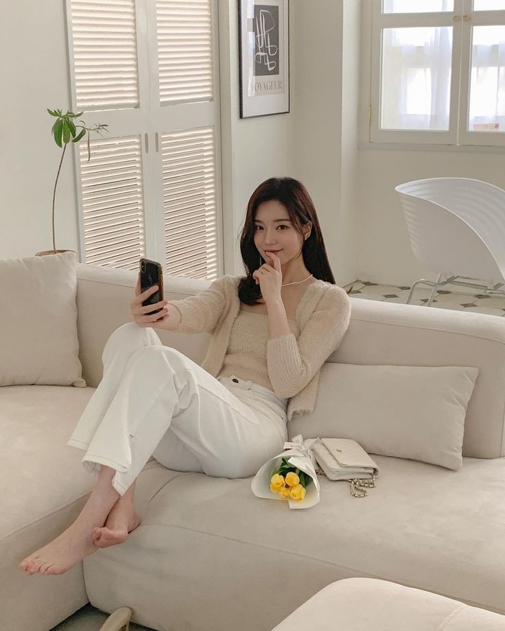 Woman in a cardigan and white pants sitting on a couch with a bouquet of flowers