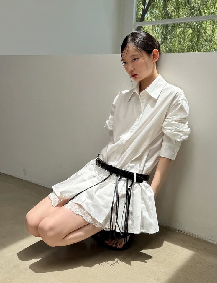 Woman in a white shirt dress with a black belt kneeling indoors