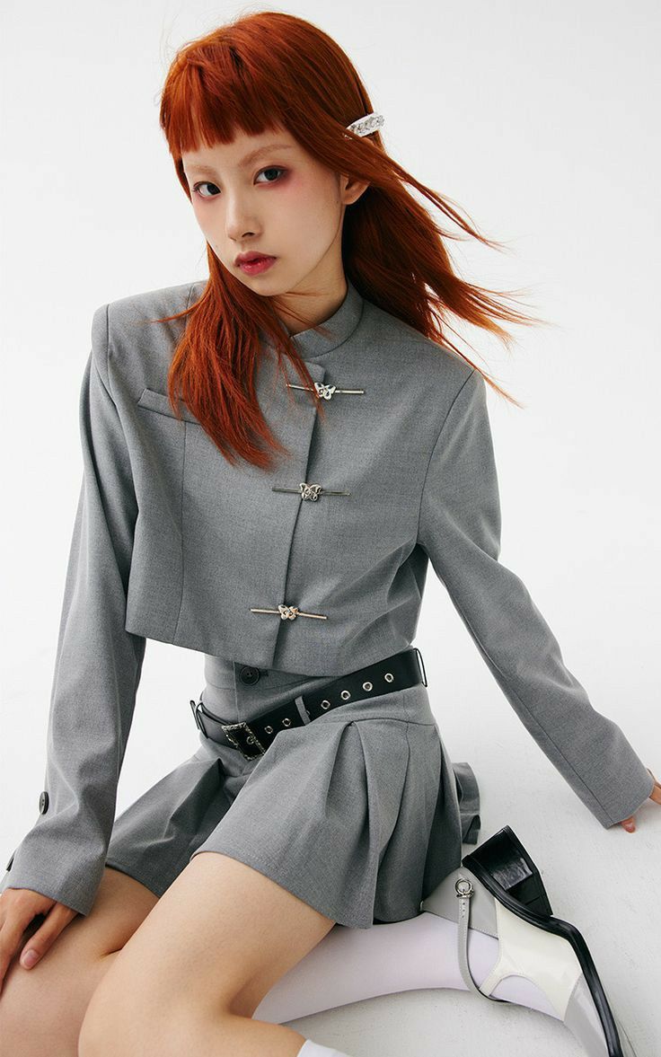 Woman with red hair in a gray cropped jacket and pleated skirt