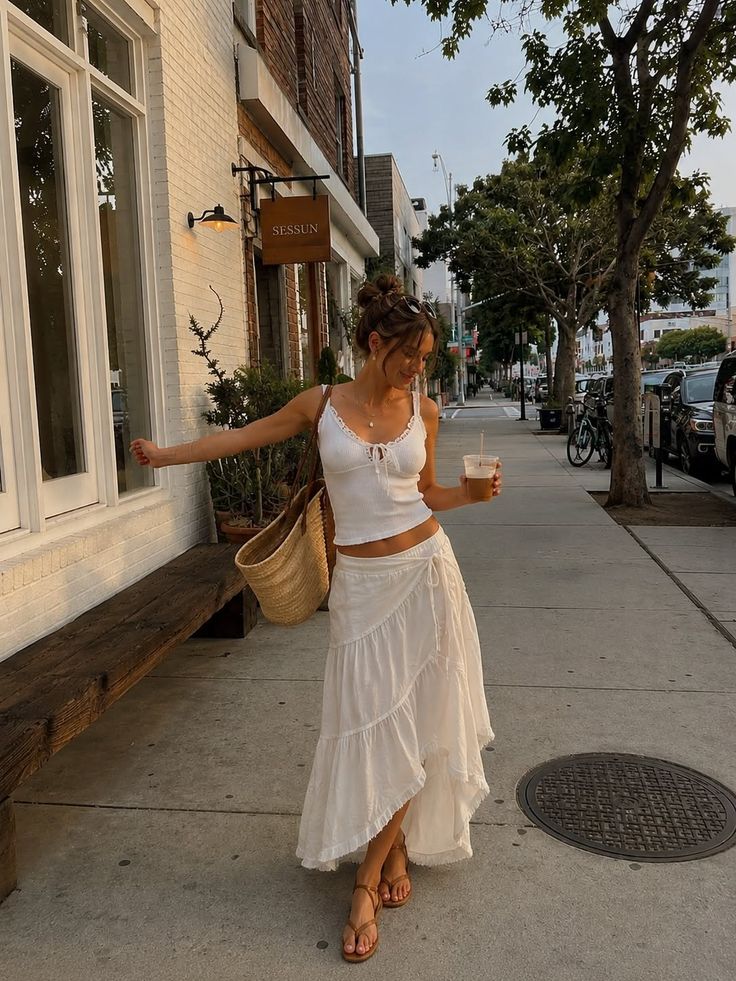 Woman in a white crop top and long skirt walking on a street at golden hour