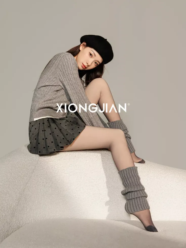 Woman in a beret, sweater, and pleated skirt with leg warmers in a studio