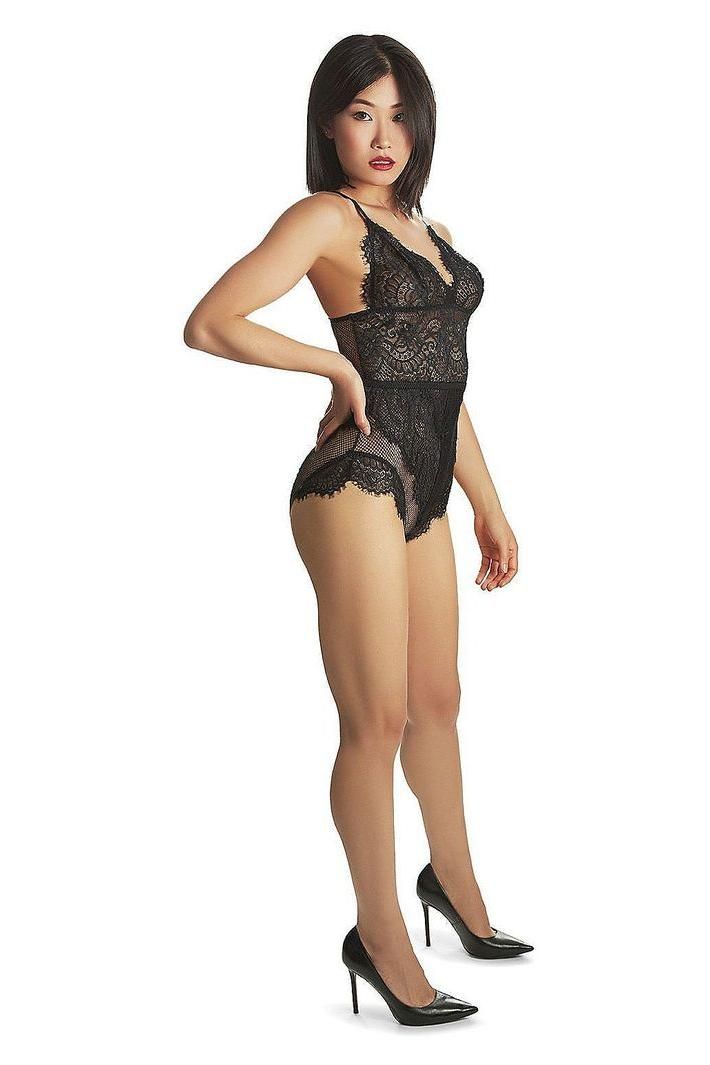 Woman in black lace lingerie and high heels posing against a white background